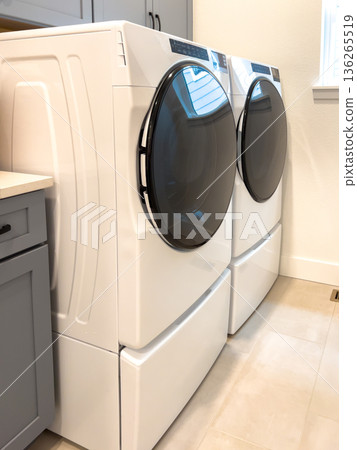 A laundry room includes a front loading washer and dryer set with a built in gray cabinet. The space is modern, functional, and clean in design. A laundry room includes a front loading washer and dryer set with a built in gray cabinet. The space is modern, functional, and clean in design. 136265519