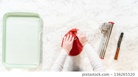 On a marble countertop, a smooth red ball of gingerbread dough is ready to be rolled. Next to the dough, a rolling pin, flour sifter, and offset spatula are arranged, creating a clean and organized On a marble countertop, a smooth red ball of gingerbread dough is ready to be rolled. Next to the dough, a rolling pin, flour sifter, and offset spatula are arranged, creating a clean and organized 136265520