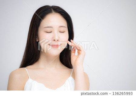 一幅展現美麗肌膚與潔淨狀態的肖像畫，畫中一位面帶微笑的日本女性雙手輕撫臉頰，雙眼緊閉。 136265993