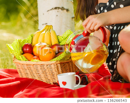 Picnic basket on blanket, woman pouring water into cup Picnic basket on blanket, woman pouring water into cup 136266543