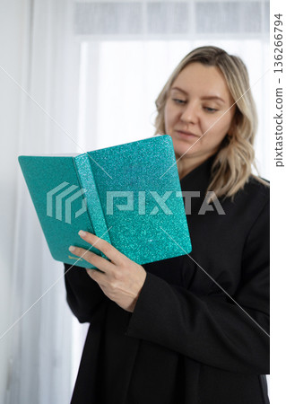 Smiling Woman Wearing Black Suit Reading a Book Indoors During Daytime 136266794