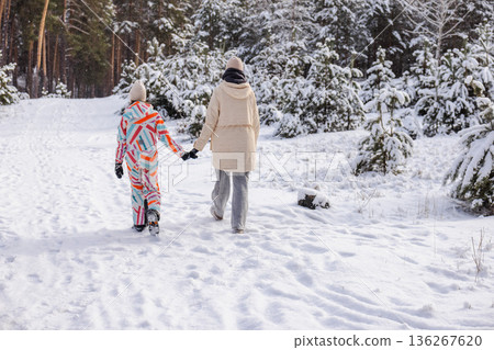 Young woman and teenage girl holding hands while walking along snowy forest path during calm winter outdoor walk Young woman and teenage girl holding hands while walking along snowy forest path during calm winter outdoor walk 136267620