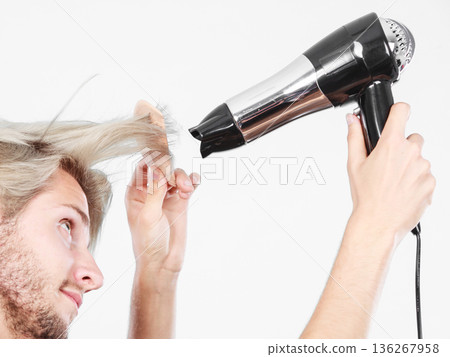 Young man drying hair with hairdryer Young man drying hair with hairdryer 136267958