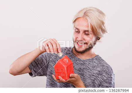 Smiling man putting coin into house piggybank 136267994