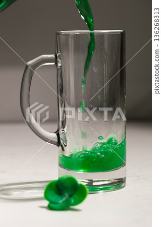Bright Green Potion Flowing Into Tall Transparent Mug With Decorative Shamrock Candies 136268313