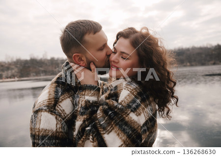 Couple shares a romantic moment outdoors on a cloudy day near a lake Couple shares a romantic moment outdoors on a cloudy day near a lake 136268630