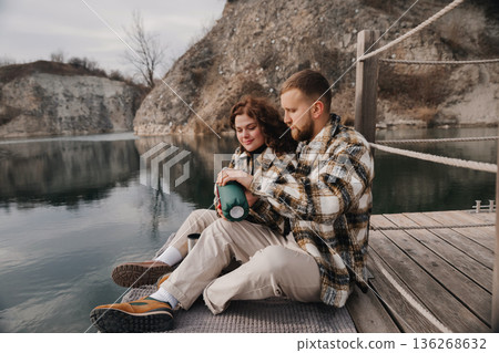 Couple sits by lake enjoying time together on Valentines Day while sharing coffee and smiles with nature all around Couple sits by lake enjoying time together on Valentines Day while sharing coffee and smiles with nature all around 136268632