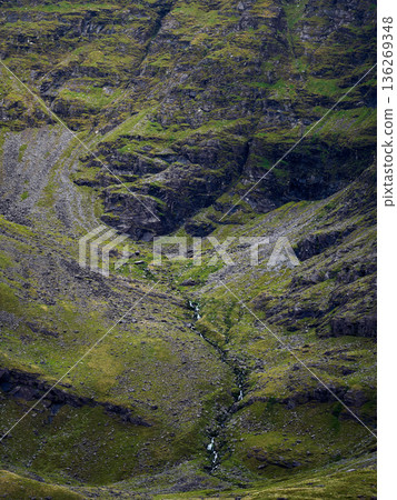 Steep mountainous landscape with green grass and small waterfalls. 136269348