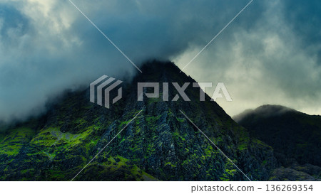 Dramatic mountain peak veiled in mist, showcasing rugged terrain and alpine vegetation under shifting clouds. Dramatic mountain peak veiled in mist, showcasing rugged terrain and alpine vegetation under shifting clouds. 136269354
