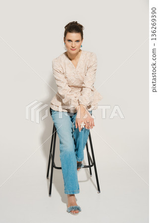 Model poses on a tall stool in a studio setting while wearing casual fashion during a photoshoot Model poses on a tall stool in a studio setting while wearing casual fashion during a photoshoot 136269390
