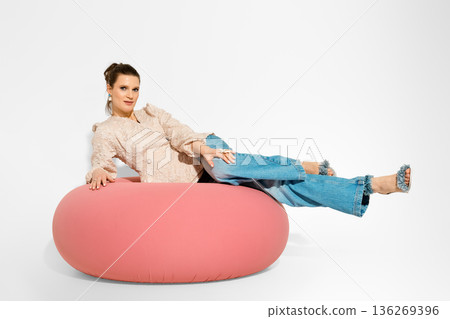 Model poses on pink lounge chair in studio setting during daytime photoshoot for fashion collection 136269396