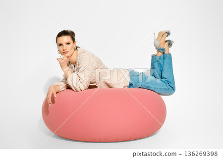 Model poses on pink cushion wearing denim jeans and heels in studio setting 136269398