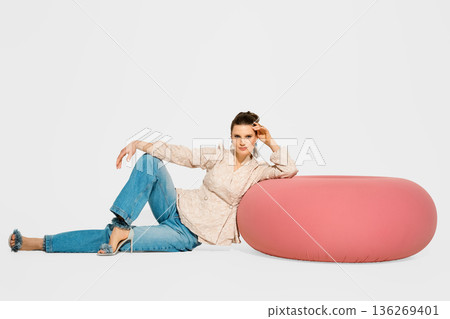 Model poses on pink furniture in studio during photo session showcasing modern fashion items 136269401