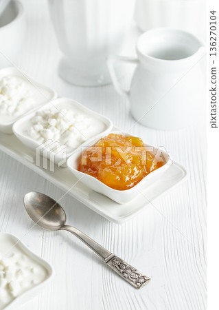 Curd dessert with cream and apricot jam on a white wooden table. 136270104