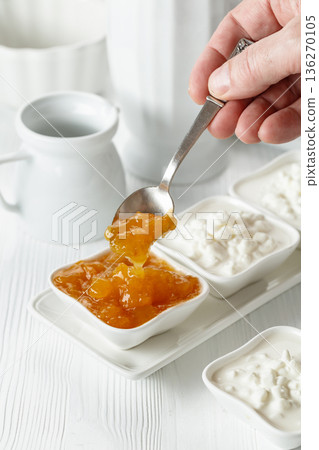 Curd dessert with cream and apricot jam on a white wooden table. 136270105