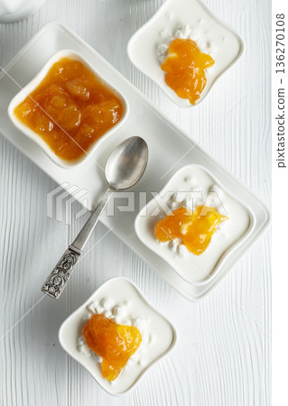 Curd dessert with cream and apricot jam on a white wooden table. 136270108