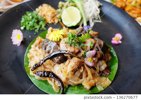 Close up stir fried rice noodle on banana leaf in black dish with Thai food on table Close up stir fried rice noodle on banana leaf in black dish with Thai food on table 136270677