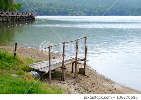 Rustic wooden bridge on riverbank with thatched building by the river for customers to dine and tropical forest background Rustic wooden bridge on riverbank with thatched building by the river for customers to dine and tropical forest background 136270686