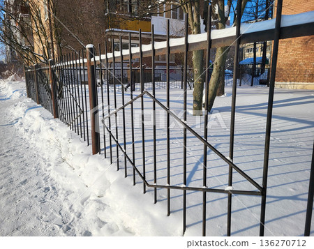 A snow-covered metal fence in the yard during the winter. A snow-covered metal fence in the yard during the winter. 136270712