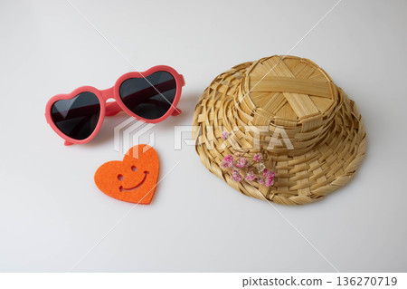 Children's heart-shaped sunglasses, a straw hat, and an orange felt heart on a light background. Summer vacation concept Children's heart-shaped sunglasses, a straw hat, and an orange felt heart on a light background. Summer vacation concept 136270719