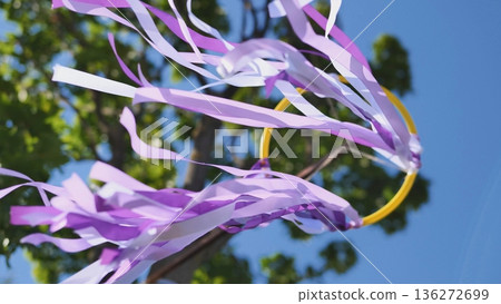 Purple ribbons dancing in wind at outdoor celebration against blue sky Purple ribbons dancing in wind at outdoor celebration against blue sky 136272699