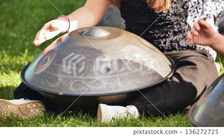 Musician playing hang drum with intricate arabic calligraphy outdoors on green grass Musician playing hang drum with intricate arabic calligraphy outdoors on green grass 136272725