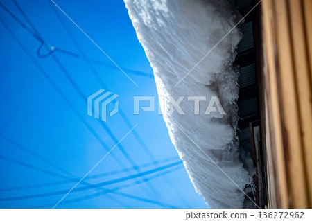 Snow falling from the roof: The danger of falling snow on a sunny day and blue skies 136272962