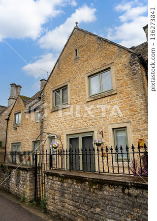 Stone houses with pitched roofs line a quiet path under a clear blue sky showing warm tones and timeless village charm in soft daylight. 136273841