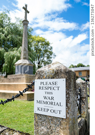 A sign requests visitors to respect the war memorial area. The notice appears on a stone post beside the monument grounds. 136273847