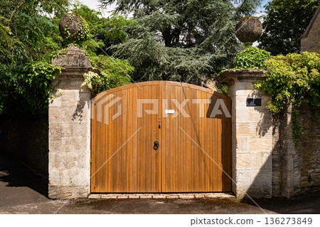 A wooden arched gate between stone pillars surrounded by greenery. 136273849