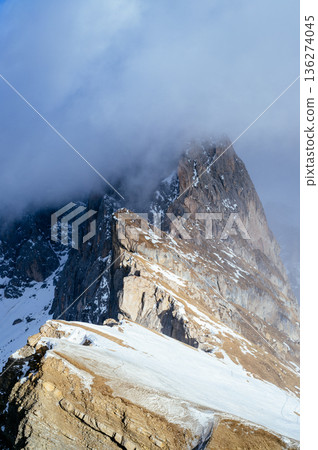 Snow covered mountain peaks emerge from clouds, revealing a dramatic alpine scene Snow covered mountain peaks emerge from clouds, revealing a dramatic alpine scene 136274045