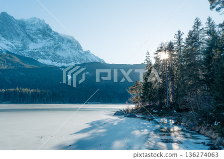 Frozen Eibsee lake, Zugspitze mountain, and sunlit pines in Bavarian winter. Idyllic landscape Frozen Eibsee lake, Zugspitze mountain, and sunlit pines in Bavarian winter. Idyllic landscape 136274063