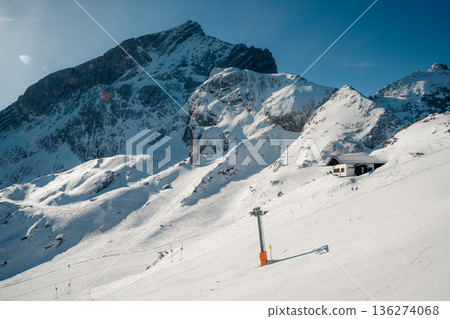 A skier descends a sunny Bavarian Alps slope with a mountain hut and ski lift 136274068