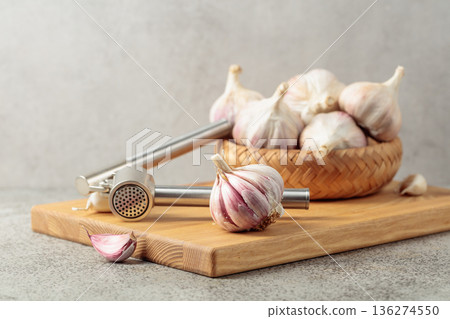 Garlic and garlic press on a wooden cutting board. 136274550