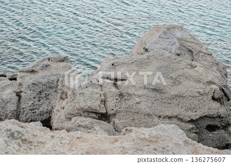 Rugged coastal limestone rocks with textured surfaces by the sea, gentle waves 136275607