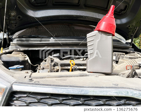 engine oil plastic bottle with red funnel cap on open car hood for maintenance 136275676