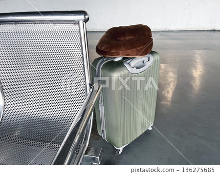 green hardshell suitcase with brown neck pillow on concrete floor near metal airport bench green hardshell suitcase with brown neck pillow on concrete floor near metal airport bench 136275685