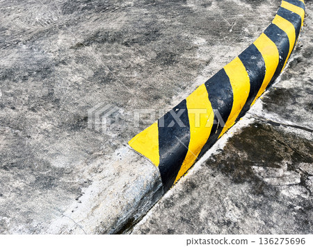 yellow and black striped concrete safety curb on sharp road curve for traffic warning 136275696