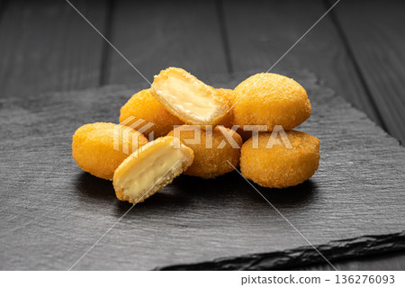 Crispy fried cheese bites with creamy filling on slate board, dark background Crispy fried cheese bites with creamy filling on slate board, dark background 136276093