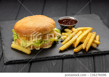 Crispy chicken burger with lettuce and melted cheese sauce, fries and ketchup , dark background 136276096