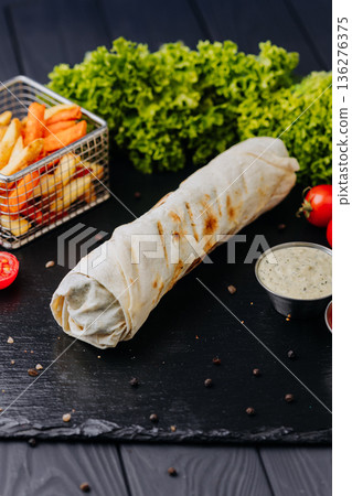 Whole shawarma wrap with fries and dipping sauces on black table Whole shawarma wrap with fries and dipping sauces on black table 136276375