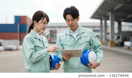 現場男女工人一起工作,同時檢查平板電腦 現場男女工人一起工作,同時檢查平板電腦 136276646