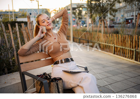 Young woman confidently talking on smartphone on city bench in Vienna 136276868