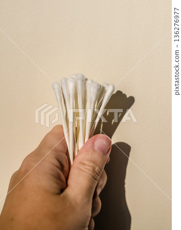 Hand holding a bunch of cotton swabs. Personal hygiene and beauty concept with minimalist background and hard shadow. Hand holding a bunch of cotton swabs. Personal hygiene and beauty concept with minimalist background and hard shadow. 136276977