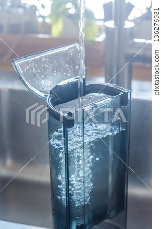 Filling a coffee machine's water tank. Pouring fresh water into the reservoir for a daily morning routine. Filling a coffee machine's water tank. Pouring fresh water into the reservoir for a daily morning routine. 136276981