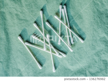 Scattered cotton swabs on a green textured background. Top view flat lay for hygiene and beauty concepts. Scattered cotton swabs on a green textured background. Top view flat lay for hygiene and beauty concepts. 136276982