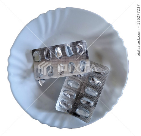 On a white plate, there are two empty packages of medicine. The packaging is metallic and shows that the capsules were removed. The setting is bright and clean. 136277237