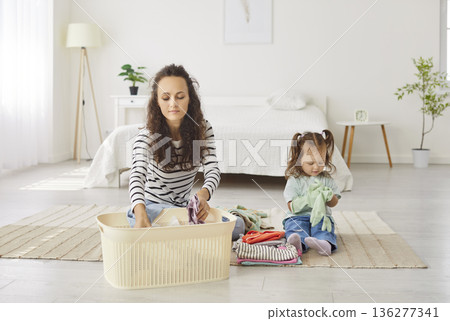 Young woman together with her cute little child sorting clothes from laundry basket 136277341
