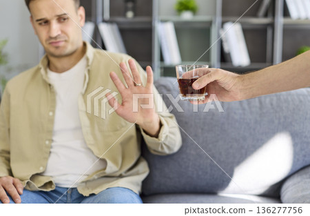 Man declines alcoholic drink on sofa, prioritizing sobriety, health, and recovery Man declines alcoholic drink on sofa, prioritizing sobriety, health, and recovery 136277756