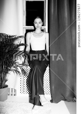 Elegant woman sitting by window in monochrome room interior 136277877